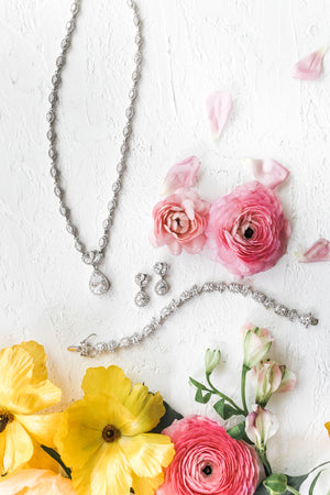 Anna Bellagio Bridal Jewelry lying on a white background with pink roses and scattered petals.