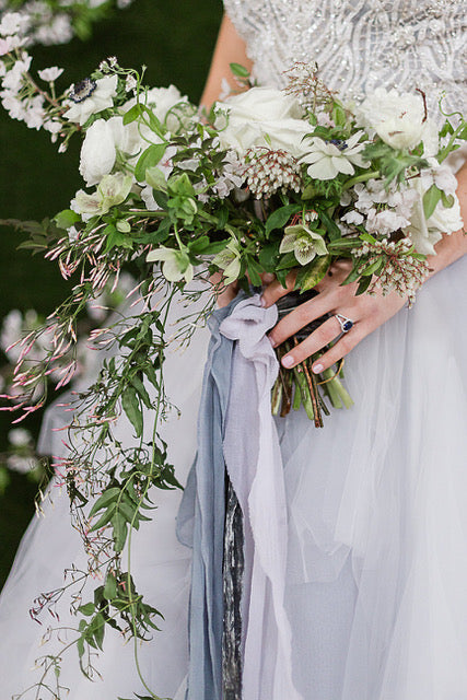 A bride wearing a light blue wedding gown holding a dramatic bouquet and wearing a sapphire wedding ring.