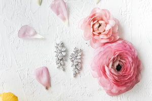 The Peony earrings with pink roses and scattered petals lying against a white background