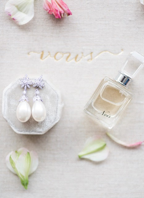 The Felina earrings and a perfume bottle with scattered rose petals against a white background
