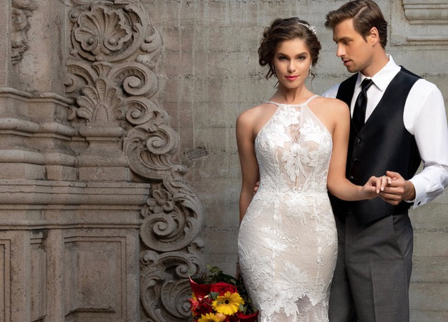 Bride and Groom holding hands standing against a gray wall. The Bride is wearing Anna Bellagio Bridal Jewelry